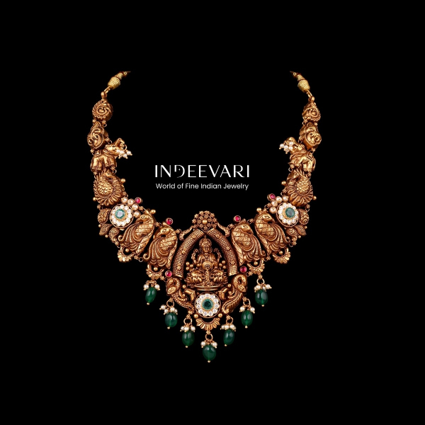 Ornate Lakshmi Mandapam Nakshi Necklace depicting goddess Lakshmi elegantly seated beneath intricate temple arch structure, surrounded by detailed peacock and floral carved motifs, antique gold finish, emerald stone accents, and green gemstone drops