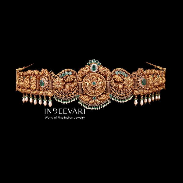 Regal Nakshi Vaddanam ornate waist belt displaying detailed peacock and floral motifs throughout, sparkling emerald green stone settings, delicate pearl drop accents, intricate filigree patterns, and symmetrical carving work in antique gold finish