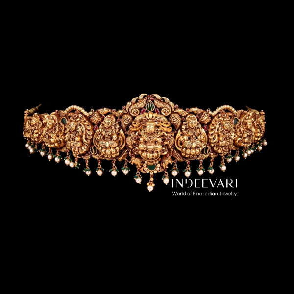Luxurious Lakshmi Nakshi Vaddanam waist belt featuring series of intricately carved goddess Lakshmi motifs accented with traditional peacock and floral details, delicate pearl lines, green bead drops, and antique gold finish throughout