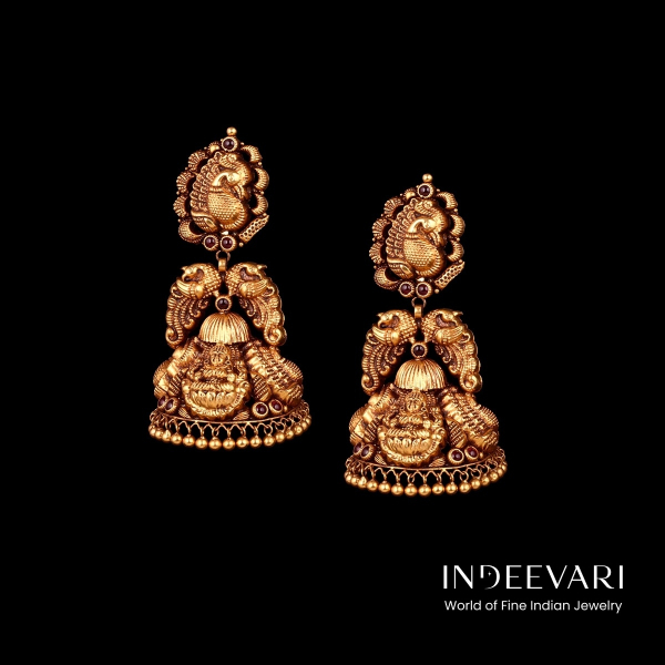Enchanting Mayura Lakshmi Nakshi Jhumkis displaying detailed peacock motifs positioned above intricately sculpted goddess Lakshmi figures, antique gold finish, ornate petal engravings, traditional ball hangings for graceful movement