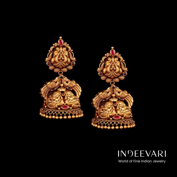 Graceful Peacock Nakshi Jhumkis featuring detailed layered peacock sculpture motifs connected by intricate floral carving and ruby stone accents, traditional dome base with elegant ball hangings, antique gold finish throughout