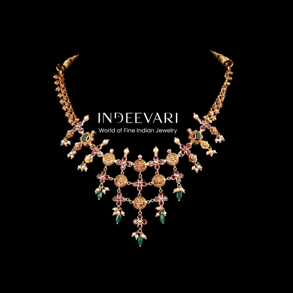 Dramatic Antique Kasu Cascade Necklace displaying rows of intricately embossed coin motifs connected with ruby and kundan floral link details, forming graceful V-shaped cascade, emerald gemstone drop hangings, delicate pearl accents, golden bead chain ele